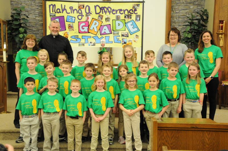 Resurrection first-graders pose in front of the traditional “Making a Difference 1st Grade Style” poster. Standing in the back row are first-grade teacher Jennifer Schmitz, left, Father Jerry Pratt, Principal Theresa Berendes, and first-grade teacher Jennifer Meyer. The Message photo by Megan Erbacher