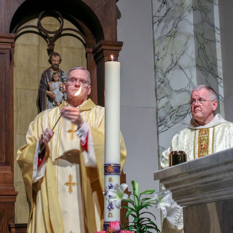 St. Benedict Cathedral Rector Benedictine Father Godfrey Mullen watches Bishop Joseph M. Siegel light the Paschal Candle at the beginning of the April 11 Easter Vigil Mass at the cathedral.